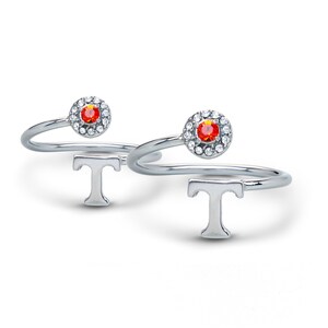 May include: Two silver rings with a red gemstone and a clear crystal halo. Each ring features a silver letter 'T' on the band.
