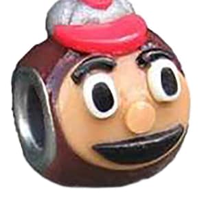 May include: A brown and white ceramic charm with a cartoon face wearing a red and white hat. The charm has a smiling face with black eyes and a black mouth.