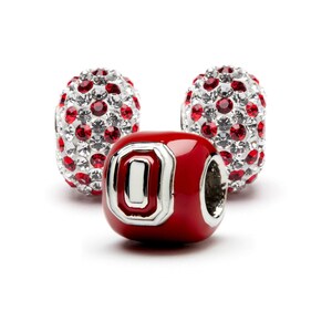 May include: Three red and silver charm beads with a white and silver letter "O" on one bead. The beads are covered in small red and clear crystals.