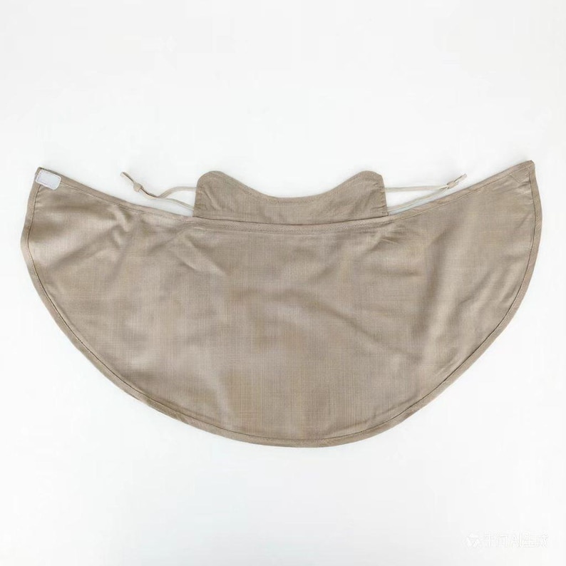 May include: A beige sun protection cape with a curved, wide brim. The cape has a neck covering and a drawstring for adjustment. The fabric appears to be a lightweight, woven material. The overall shape is designed to shield the neck and shoulders from the sun.