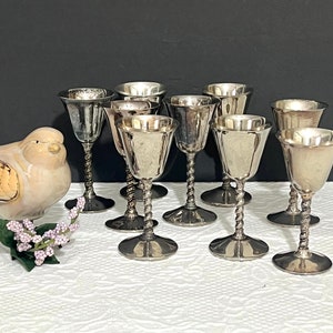 May include: Set of eight silver-plated goblets with twisted stems. The goblets are arranged in a semi-circle on a white surface.