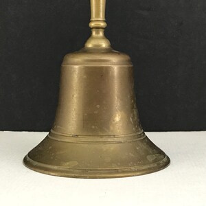 May include: A brass bell with a rounded top and a flared base. The bell has a smooth, aged finish with a slight patina.