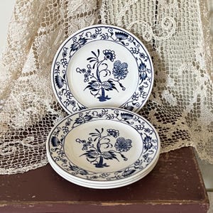 Op de afbeelding: Vier witte keramische borden met een blauw bloemenmotief. De borden hebben een blauwe rand en een blauw bloemenmotief in het midden.