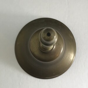 May include: A vintage brass bell with a round base and a knob on top. The bell has a worn, aged finish.