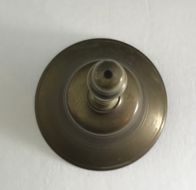 May include: A vintage brass bell with a round base and a knob on top. The bell has a worn, aged finish.