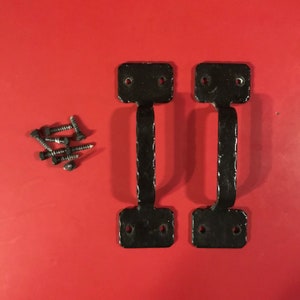 May include: Two black metal door handles with square plates and a hammered finish. The handles are attached to a red surface with screws.