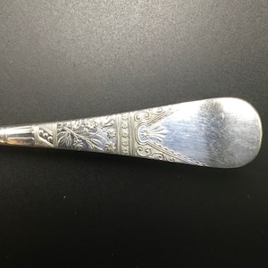 Op de afbeelding: Close-up van de achterkant van een zilveren lepel met een sierlijk bloemmotief.