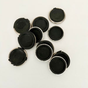 Puede incluir: Un conjunto de diez protectores de muebles de color plateado con almohadillas de goma negra. Los protectores son redondos y tienen una superficie lisa.