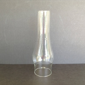 May include: A clear glass lamp chimney with a flared, hourglass shape. The glass is transparent, allowing light to pass through. The chimney has a rounded base and a slightly wider top.