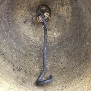 May include: Close-up of the inside of a brass bell with a black metal clapper attached to the top.