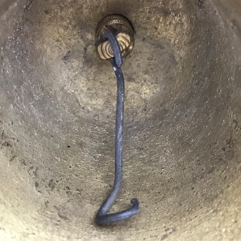 May include: Close-up of the inside of a brass bell with a black metal clapper attached to the top.