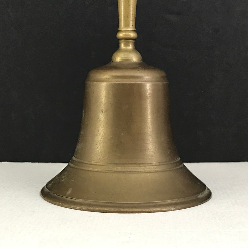 May include: A brass bell with a rounded base and a smooth, polished finish. The bell has a simple, elegant design.