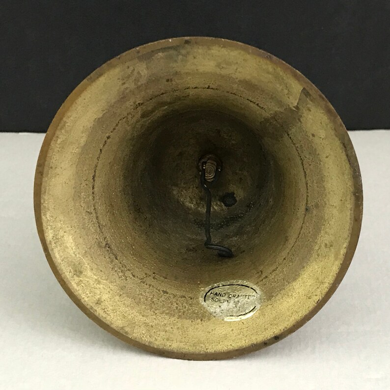 May include: A brass bell with a black metal clapper and a sticker that reads "Hand Crafted Solid Brass".
