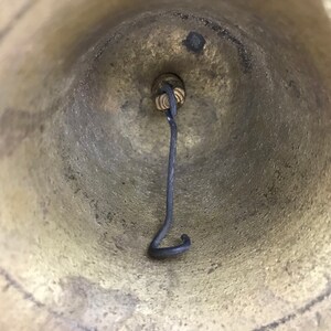 May include: The inside of a brass bell with a black metal hook attached to the top.