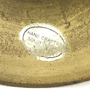 May include: Close-up of a brass object with a white oval sticker that reads "HAND CRAFTED SOLID".