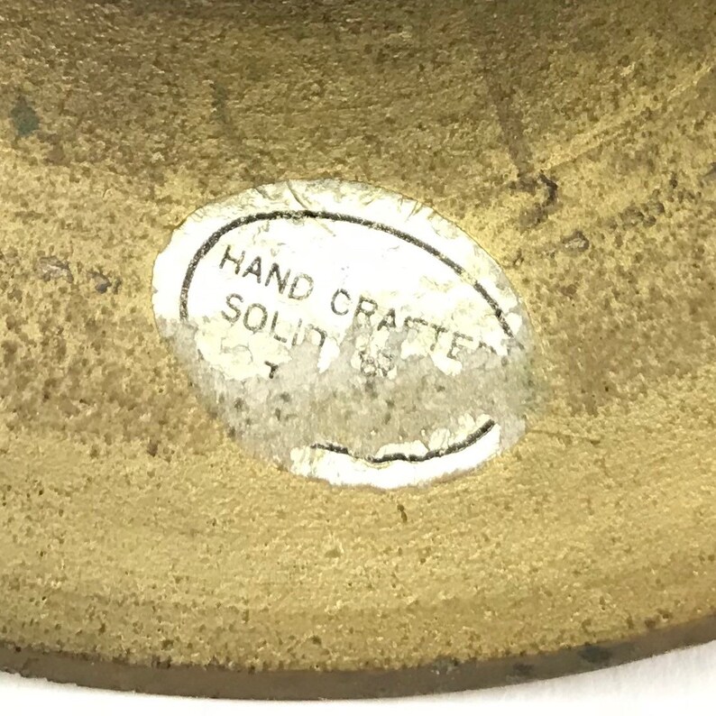 May include: Close-up of a brass object with a white oval sticker that reads "HAND CRAFTED SOLID".