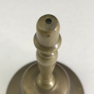 May include: A brass bell with a round base and a tall, slender stem. The bell has a small opening at the top.