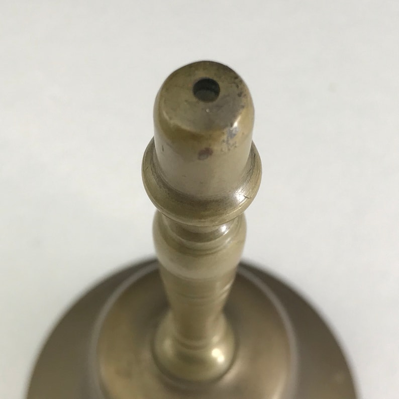 May include: A brass bell with a round base and a tall, slender stem. The bell has a small opening at the top.