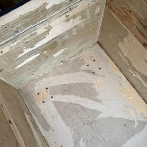 Puede incluir: Vista interior de una caja de madera, mostrando las paredes y la base. La madera tiene un aspecto envejecido con pintura descascarillada y clavos visibles. La caja est&aacute; vac&iacute;a, revelando su construcci&oacute;n y edad.