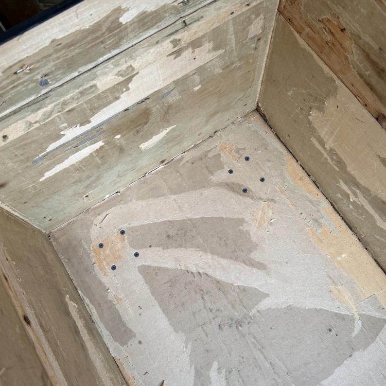 Puede incluir: Vista interior de una caja de madera, mostrando las paredes y la base. La madera tiene un aspecto envejecido con pintura descascarillada y clavos visibles. La caja est&aacute; vac&iacute;a, revelando su construcci&oacute;n y edad.