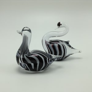May include: Two glass swans with black and white striped patterns. The swans are facing each other with their necks curved.