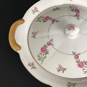 Puede incluir: Plato de servir de cerámica blanca con tapa, con borde dorado y un delicado patrón floral de rosas rosas y hojas verdes.