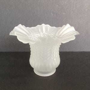 May include: Frosted glass lampshade with a ruffled edge. The shade has a textured, patterned design on the body and a flared, scalloped top. The lampshade is white and has a classic, vintage aesthetic.