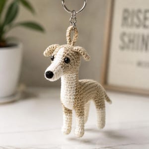 Puede incluir: Un llavero de ganchillo con forma de perro pequeño hecho de hilo beige y blanco. El perro tiene el pecho, el hocico y la parte inferior de las patas de color blanco, con color beige en el lomo, la cabeza y las orejas. Tiene dos ojos de cuenta negra.