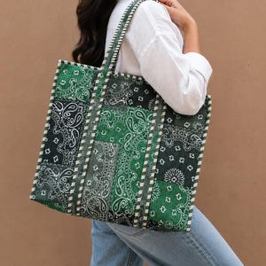 Peut inclure: Un sac fourre-tout rectangulaire présentant un motif patchwork de style bandana vert et noir avec des imprimés cachemire. Le sac est fabriqué en tissu matelassé et comprend deux bandoulières avec une bordure rayée blanche et verte.