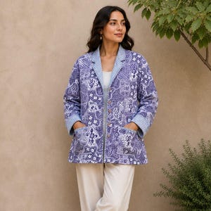 May include: A long-sleeved quilted jacket featuring a blue and white intricate paisley pattern, a notched collar with blue and white striped trim, two front patch pockets, and a button-down front, paired with plain off-white trousers and brown sandals.