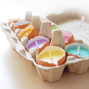 Könnte beinhalten: Sechs bunte Kerzen in Eierschalen, angeordnet in einem Eierkarton aus Pappe.