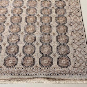 Peut inclure: Tapis beige et marron à motifs géométriques répétitifs. Le tapis présente une série de formes octogonales dans des tons de marron et de beige, avec une bordure en forme de losanges. Le tapis a une bordure frangée et le texte "TheAntiqueRug".