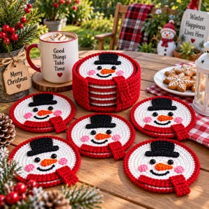 May include: A set of round, crocheted snowman coasters featuring a white face, black top hat, orange carrot nose, and red scarf. The coasters are stacked in a matching red crocheted holder, with individual coasters displayed on a wooden surface.