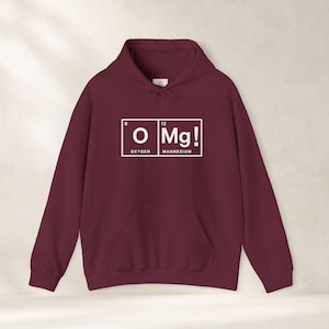Peut inclure: Un sweat-shirt à capuche bordeaux à manches longues avec une impression graphique blanche représentant deux éléments du tableau périodique. Le motif affiche la lettre O avec le chiffre 8 et le mot OXYGEN, à côté de Mg avec le chiffre 12 et MAGNESIUM.