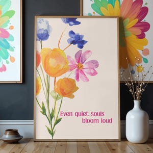 Könnte beinhalten: Ein gerahmter Kunstdruck mit einem Aquarell-Blumenmuster in Orange, Rosa und Blau. Der Druck enthält den Text "Even quiet souls bloom loud" in Rosa. Das Kunstwerk wird zusammen mit anderen gerahmten Kunstwerken ausgestellt.