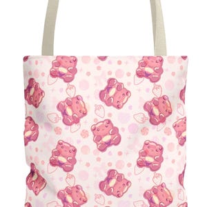 Könnte beinhalten: Hellrosa Tragetasche mit einem sich wiederholenden Muster aus rosa Gummibärchen, Erdbeeren und Süßigkeiten auf weißem Hintergrund. Die Tasche hat einen hellbeigen Griff.