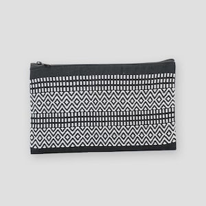 Peut inclure: Une pochette zippée à motifs noirs et blancs. La pochette présente un motif géométrique avec des rangées de points blancs et des losanges sur fond noir. La fermeture éclair est noire.
