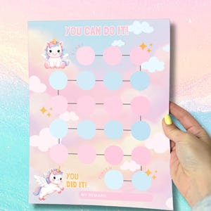Peut inclure: Un tableau aux couleurs pastel sur le thème des licornes. Le tableau comporte des cercles roses et bleus pour suivre les progrès, avec les phrases "You Can Do It!" et "You Did It!" imprimées dessus. Le tableau est tenu par une personne.
