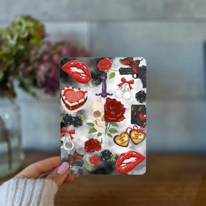 Peut inclure: Une carte rectangulaire présentant un collage d'illustrations sur un fond gris fumé. Les éléments incluent un crâne et une épée au centre, des roses rouges, des lèvres rouges, des papillons noirs, des menottes, un pistolet et des cœurs.