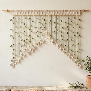 Peut inclure: Un rideau en crochet de couleur crème avec une tringle en bois. Le rideau présente des brins verticaux avec des feuilles vertes et des fleurs de couleur crème. Les fleurs sont disposées en diagonale. C'est un élément de décoration intérieure.