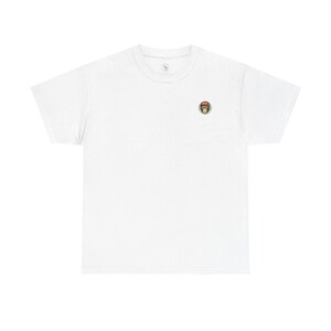 Könnte beinhalten: Ein weißes T-Shirt mit einem kleinen, kreisförmigen, gestickten Aufnäher mit einem Affengesicht. Der Aufnäher hat ein braunes Affengesicht mit gelbem und grünem Rand. Das Shirt hat einen Rundhalsausschnitt und kurze Ärmel.