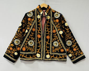 Puede incluir: Chaqueta negra con intrincados bordados florales en dorado, naranja y blanco. La chaqueta presenta un cuello con muescas y un forro a rayas rojas y blancas. El bordado crea un diseño detallado y ornamentado.