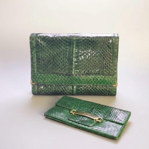 May include: Two green leather wallets. The larger wallet is rectangular with a flap closure and gold-colored hardware. The smaller wallet is rectangular with a flap closure and gold-colored hardware. The wallets have a snakeskin pattern.