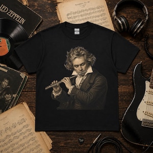 Può includere: Una t-shirt nera a maniche corte con una stampa grafica color seppia raffigurante un uomo dai capelli mossi che indona un cappotto e una cravatta d'epoca mentre suona un flauto d'argento. La maglia presenta un classico girocollo.