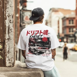 Könnte beinhalten: Weißes T-Shirt mit einem Grafikdesign mit einem Auto, japanischem Text und einer roten Sonne. Das Design enthält die Wörter "DRIFT CULTURE" und "SLIDE OR DIE". Das T-Shirt wird im Freien getragen.