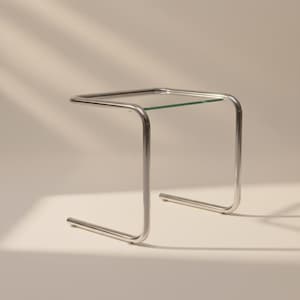 May include: A modern side table with a clear glass top and a polished chrome frame. The table has a square top and a curved, tubular metal base. The overall design is minimalist and sleek, suitable for various interior styles.