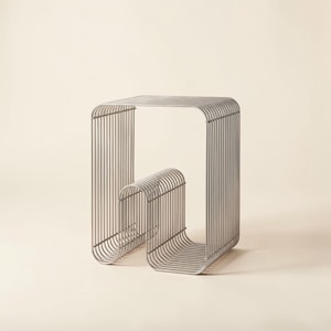 May include: A modern, silver-colored metal side table with a unique, curved design. The table features a rectangular top and a base constructed from vertical metal rods, creating an open, airy aesthetic. The table's dimensions are approximately 18 inches in height and 14 inches wide.