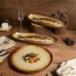 Puede incluir: Dos fuentes ovaladas de cerámica con centro beige y borde marrón oscuro, cada una con un pescado entero cocinado y adornado con hierbas. Un plato redondo grande de cerámica con acabado beige y marrón a juego contiene una porción de verduras.