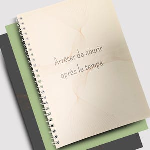 May include: A spiral-bound notebook with a cream-colored cover featuring the text "Arrêter de courir après le temps" in a light brown font. The notebook is layered over a green and a dark gray notebook.