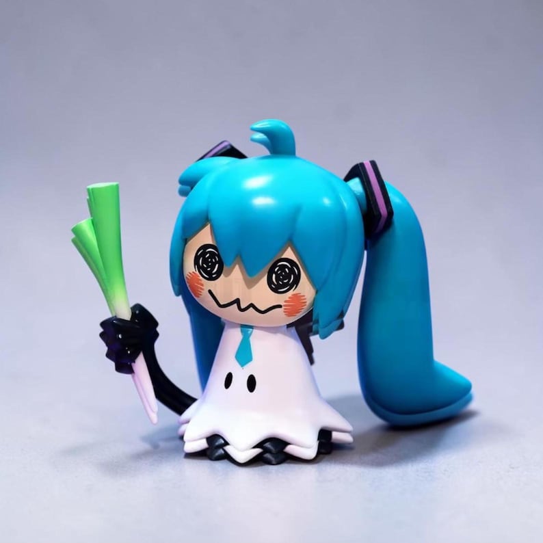 以下が含まれることがあります： 明るいターコイズ色の髪の毛をツインテールにしたキャラクターのフィギュア。緑色の野菜を持っています。白いドレス、黒い腕、渦巻きの目とバラ色の頬を持つ漫画の顔をしています。明るい灰色の背景にあります。